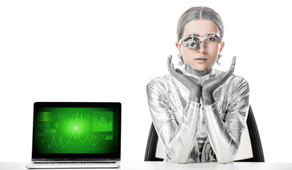 silver robot sitting at table near laptop with business appliance isolated on white, future technology concept