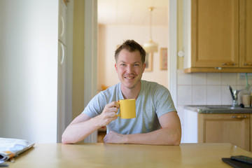 Fototapeta na wymiar Young Happy Man Sitting And Drinking Coffee By The Window