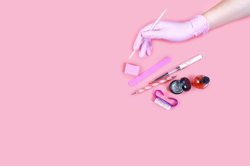 manicure and pedicure equipment. master nails in pink gloves holds manicure tool on the pink background. flat lay composition for card with a place for text