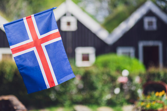 Iceland, Iceland national flag in the foreground, typical Icelandic houses with grass on the roof in the background
