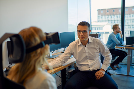 Man looking at woman wearing VR glasses in office