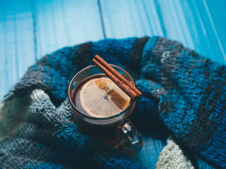 A mug of hot tea with cinnamon on a blue background with a scarf
