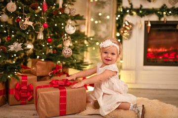 Obraz na płótnie Canvas baby happiness little girl rejoices christmas under the tree fireplace and gifts