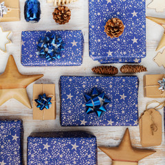 Creative chritmas composition. Presents in dark blue wrapping paper with silver stars and sparkles, wooden decorations, ornaments, paper tags on white table, overhead view, selective focus