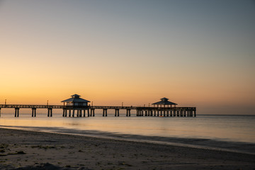 fort myers beach pier with flat water before sunrise, orange light at the horizon