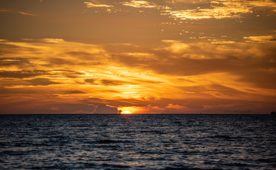 sunset over the sea, orange sun half in the water with sunlit clouds