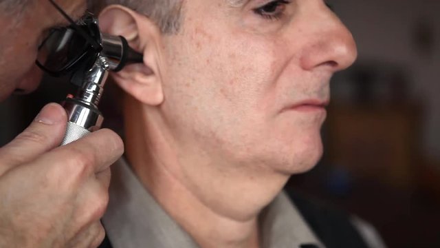 A doctor examines a senior man's ear with an otoscope in a home environment.