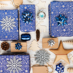 Creative chritmas composition. Presents in dark blue wrapping paper with silver stars and sparkles, wooden decorations, ornaments, paper tags on white table, overhead view, selective focus