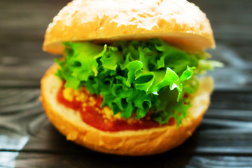 Close up of burger filled with meat, salad, tomatoes and mustard on rustic vintage dark wooden background