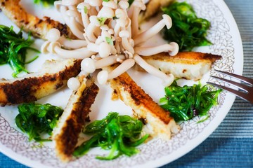 Fried sliced fish, seaweed and shimeji mushroom on plate,closeup.
