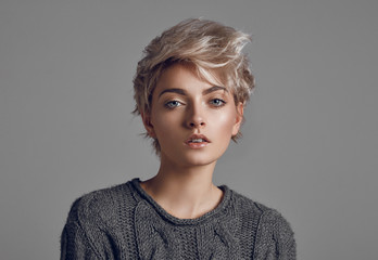 Fashion portrait of young woman with blond short hair isoalted on gray background