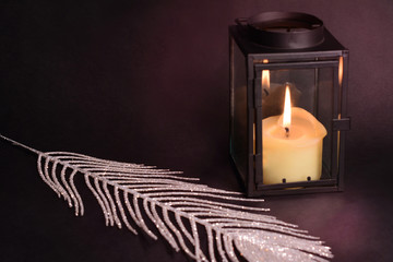 Christmas decoration on black background. Lantern, candle, silver feather