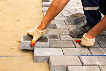 Laying gray concrete paving slabs in house courtyard driveway patio. Professional workers bricklayers are installing new tiles or slabs for driveway, sidewalk or patio on leveled sand foundation base