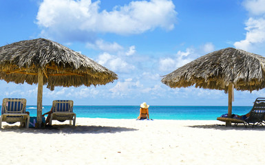 Cabana, parasol. White sand beach. Blue sea water and dramatic clouds. Oranjestad, Aruba. Famous Eagle Beach.  Unidentifiable sun bather.