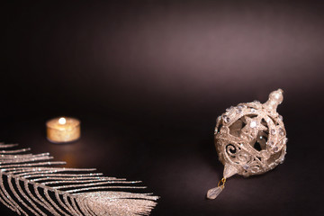 Christmas decoration on black background. Candle, silver feather and christmas tree bauble