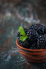 Blackberries in a ceramic bowl on wooden background close up. Rustic style