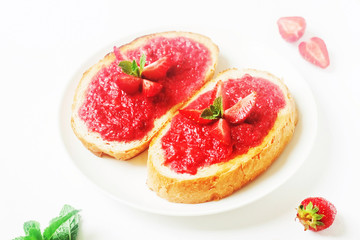 Slices of french bread with strawberry jam and mint on white background - healthy summer breakfest
