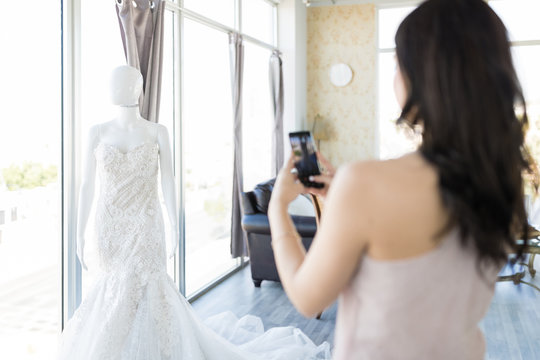 Bride Taking Picture Of Elegant Gown In Bridal Shop