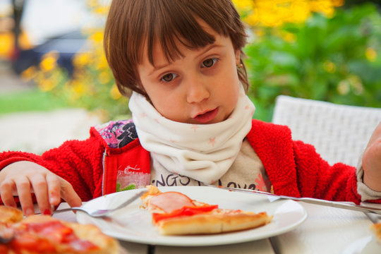 Little female child with pizza slices in front of their faces. Happy cule little girl having fun eating dinner.