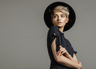 Fashion portrait of female model with blond short hair wear black hat and looking at empty space