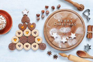 Original Christmas tree made of heart shape cookies and Ingredients for Christmas Baking on concrete light blue table. Top view, close-up.  Christmas, New Year concept
