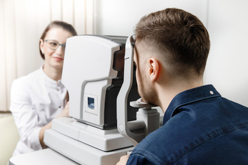 Female doctor ophthalmologist clinic checks eye vision of man on machine lamp.