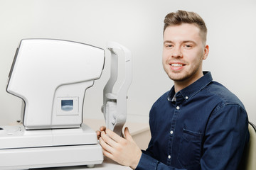 Young man smiles reception doctor ophthalmologist to check eyes of patient on device