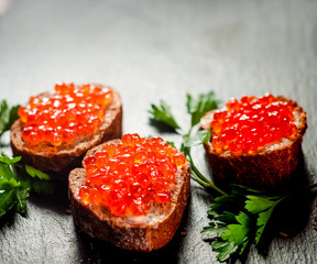 Red caviar on bread on slate background.