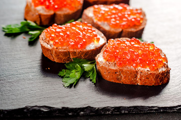 Red caviar on bread on slate background.