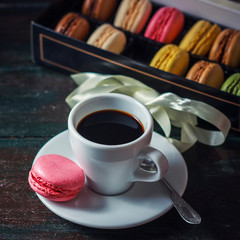 Beautiful breakfast. Morning cup of coffee with colorful macarons, on with flowers on dark background with copy space.