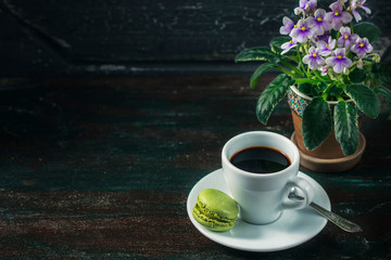 Beautiful breakfast. Morning cup of coffee with colorful macarons, on with flowers on dark background with copy space.