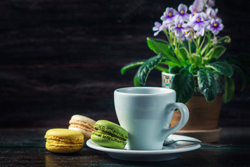 Beautiful breakfast. Morning cup of coffee with colorful macarons, on with flowers on dark background with copy space.