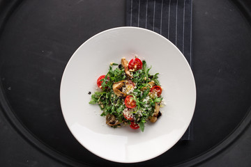 Salad with mushrooms, tomatoes and greens on black background.