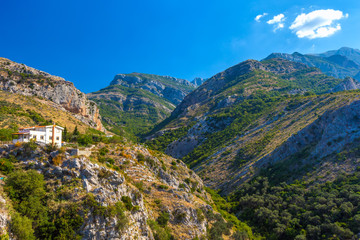 Fototapeta na wymiar White house on the slope of a beautiful colorful mountain in front of the gorge opposite other side of the canyon on a sunny day with a blue sky. Summer landscape in Fortress Old Bar Town, Montenegro.