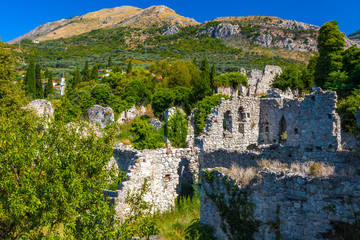 The picturesque historic walls of the destroyed city covered with green plants grass trees on the backdrop of colorful mountains and clear sky. Summer landscape in Fortress Old Bar Town, Montenegro.