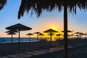 Sunset with colorful sun rays on the shore of the Adriatic Sea, paths sunbeds and umbrellas made of wood and straw in the recreation area on the sand. Beach on Ada Bojana, Ulcinj, Montenegro.