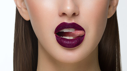 Close-up of sexy female lips with tongue. Clean skin and a clear lip contour are outlined with a fashionable marsala lipstick. White teeth and the beauty of smile for stamotologii, spa or cosmetology