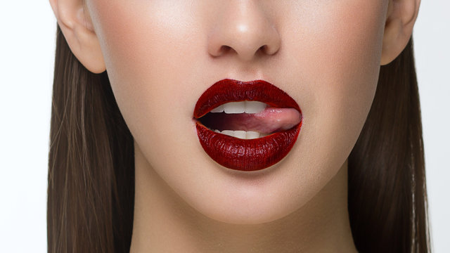 Close-up of sexy female lips with tongue. Clean skin and a clear lip contour are outlined with a fashionable red lipstick. White teeth and the beauty of a smile for stamotologii, spa or cosmetology