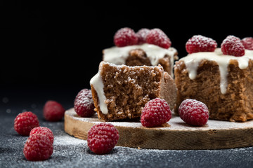 The home-made simple cake with the glazed surface decorated with fresh berries of raspberry. Cake is cut on portion pieces and laid out on a wooden support. A black background, it is isolated