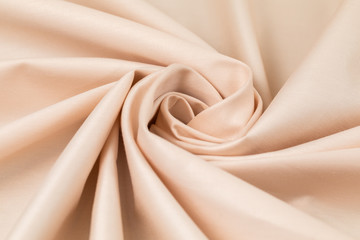 Sateen fabric, cream with pink shade, is draped with diagonal folds in the form of a spiral
