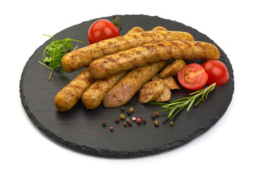 Delicious BBQ Sliced Sausages with herbs and tomatoes on a slate shale plate, isolated on a white background. Close-up.