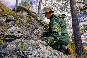 Fototapeta na wymiar geologist using a geological hammer takes a rock sample outdoor