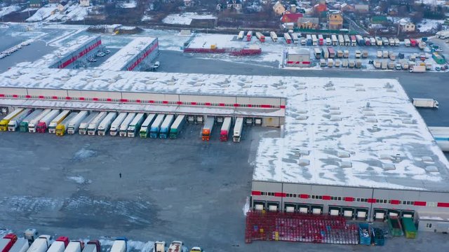 Aerial circling view of the warehouse logistics centre with parked semi-trailer trucks in winter day