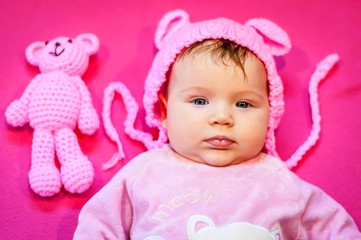 Sweet and adorable blue eyed Caucasian three months old newborn infant baby girl with a pink teddy bear isolated on a pink background. It's a girl concept. Infant with a serious look idea.