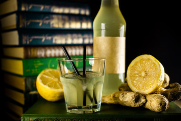 Bottle and glass with craft lemon-ginger alchol drink on background with books. Vertical photo.
