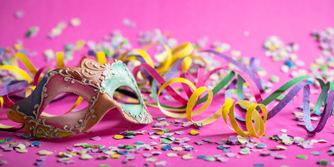 Carnival mask, streamers and confetti on bright pink background