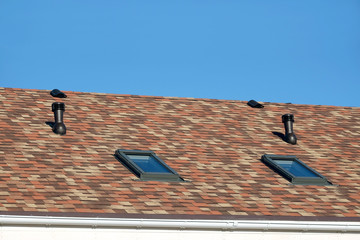 Roof windows and ventilation tubes on residential house covered with motley soft shingles close up...