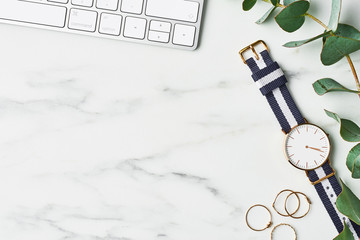 Business composition with white computer keyboard, eucalyptus plant, women's watch and golden rings on white marble background. Office concept. Top view with copy space for text.