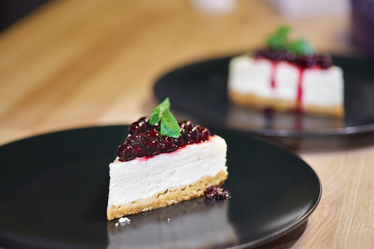 Piece of cheesecake with black currant and blueberry sauce on white plate on wooden table