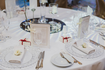 Round table served with empty plates, knives, forks, card and napkins, covered with white tableclothes. Cutlery, glassware on festive table.